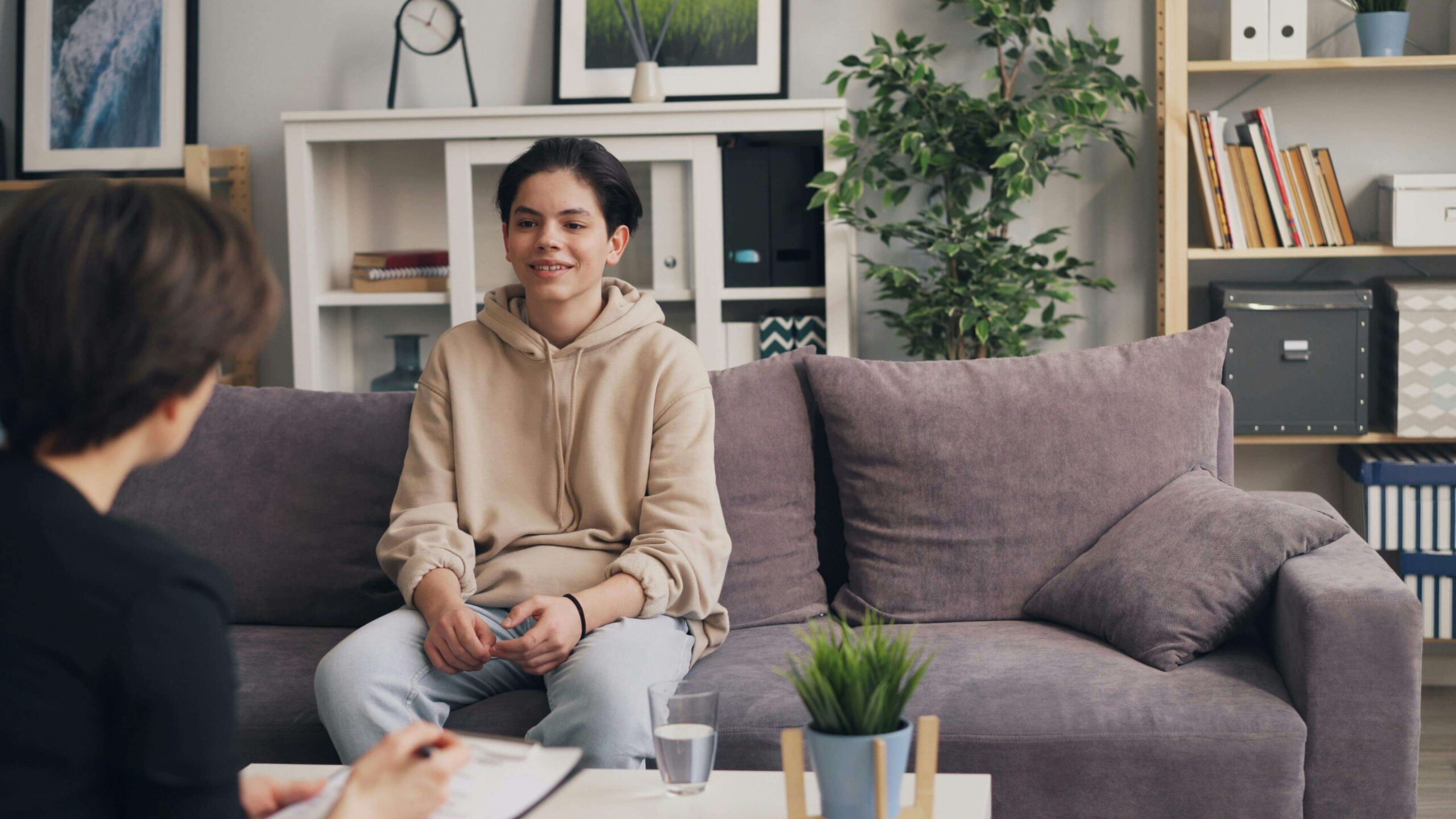 Smiling teenager sitting on couch in therapy session with therapist.